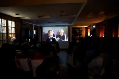 Stemningsfull filmvisning av Babettes Gjestebud ved Strand Hotel Fevik. Gjester ser film ved bord med levende lys.